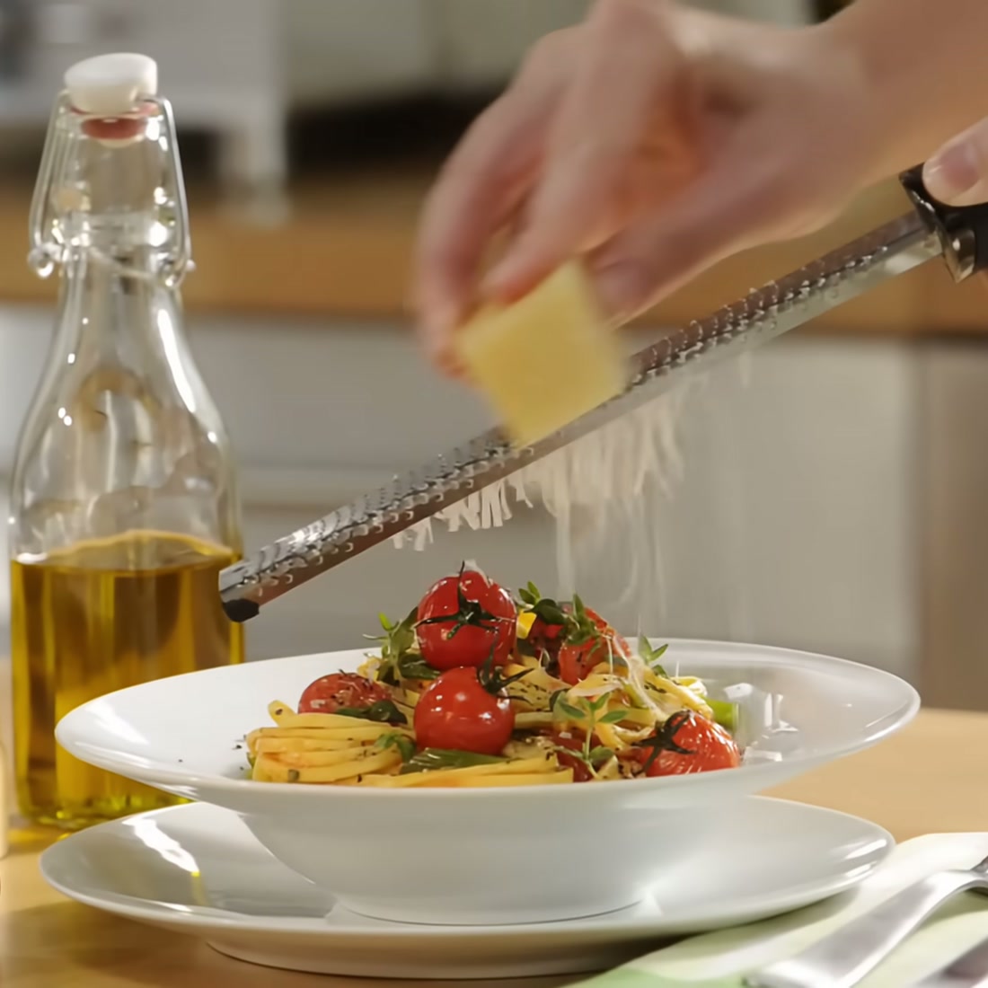The Microplane zester grating fine Parmesan shreds over a bowl of pasta